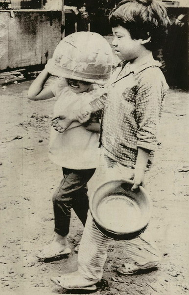Để bảo vệ bản thân mình khỏi đạn lạc, một em bé đội trên đầu chiếc mũ của lính Mỹ, trong khi em kia thủ trong tay chậu nhôm. Ảnh chụp ngày 14/7/1972.
