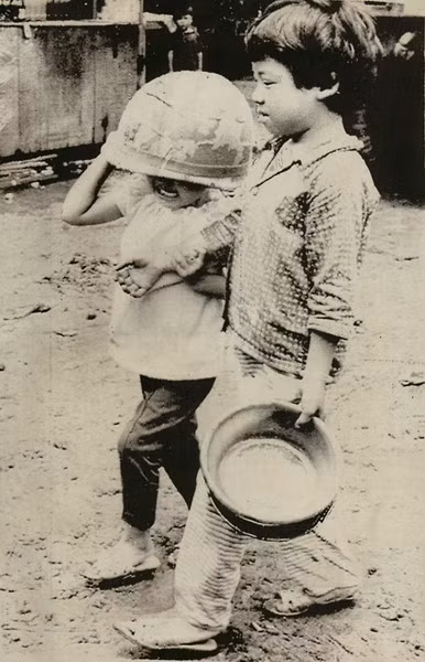 Để bảo vệ bản thân mình khỏi đạn lạc, một em bé đội trên đầu chiếc mũ của lính Mỹ, trong khi em kia thủ trong tay chậu nhôm. Ảnh chụp ngày 14/7/1972.