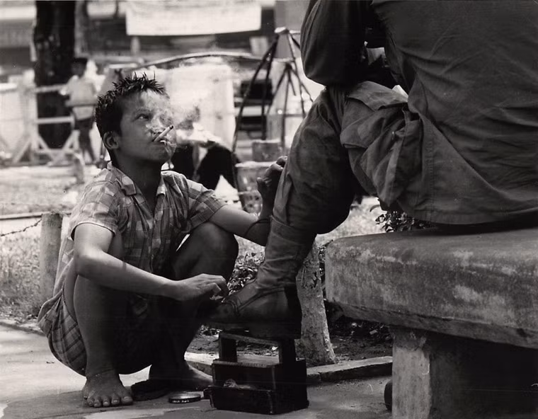 Cậu bé người Việt vừa phì phèo thuốc lá vừa đánh giày cho một lính Mỹ ở Sài Gòn năm 1968.