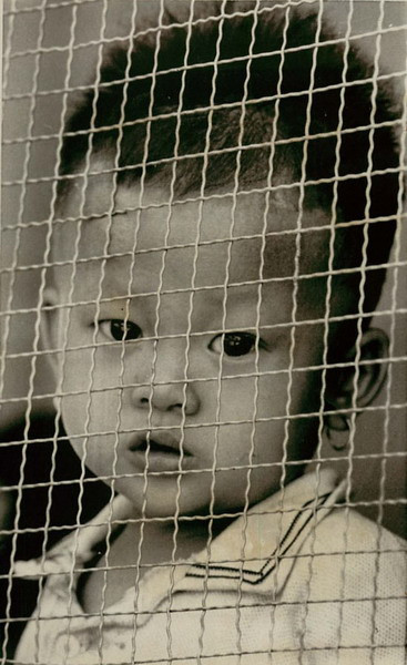 Ngày 15/4/1973, một em bé nhìn vào ống kính máy ảnh qua ô cửa chăng lưới sắt của một trại tập trung ở Bình Dương, nơi mẹ em - một chiến sĩ giải phóng - bị giam giữ.