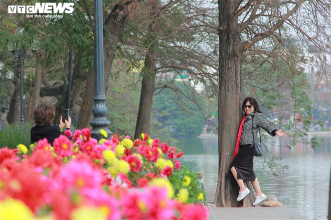 Người phụ nữ không đeo khẩu trang đứng tạo dáng chụp ảnh bên Bờ Hồ.