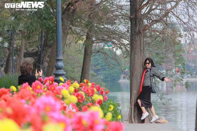 Người phụ nữ không đeo khẩu trang đứng tạo dáng chụp ảnh bên Bờ Hồ.