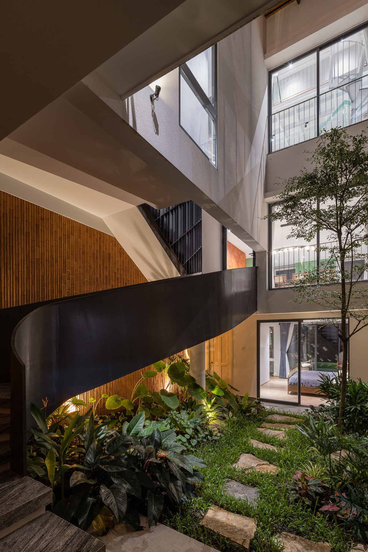 Một mảng vườn nhỏ trải đầy cây xanh mang đậm chất Tropical làm nổi bật mảng tường gạch đỏ được ốp dọc theo chiếc thang xoắn hướng lên phòng bếp.