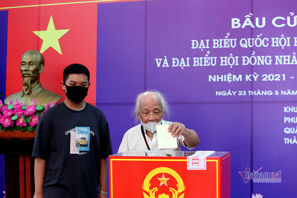 Tại điểm bỏ phiếu phường Hàng Bài - quận Hoàn Kiếm, các cử tri xếp hàng giữ khoảng cách, đo thân nhiệt, xịt cồn trước khi vào bỏ phiếu thực hiện quyền công dân.