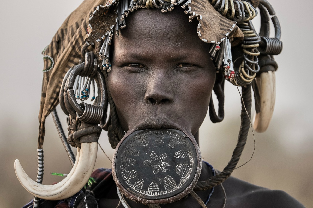 Đeo đĩa môi là một trong những tập tục có từ thời nguyên thuỷ của bộ lạc Mursi ở châu Phi. Đường kính đĩa càng lớn thì địa vị xã hội của cô gái càng cao, đồng nghĩa số của hồi môn khi về nhà chồng càng lớn. Người Mursi tin chiếc đĩa sẽ ngăn chặn các linh hồn ma quỷ xâm nhập vào cơ thể qua miệng. Họ cũng thích đội sừng động vật lên đầu, với ý nghĩa trong quá khứ là phản đối chế độ nô lệ, giờ chỉ đơn giản là làm đẹp.