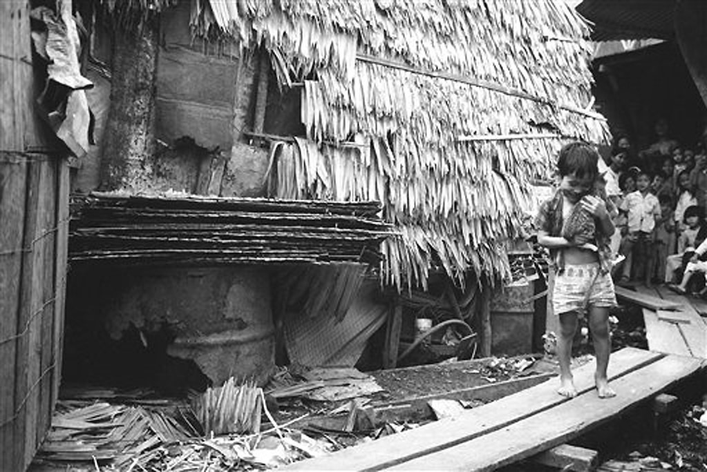 Chú bé ôm mèo cưng, đứng ở lối đi bằng ván gỗ bắc trên dòng nước thải bốc mùi khó chịu ở khu Mả Lạng. Ít ai ngờ rằng cách đó không xa là những đường phố sang trọng của đô thành Sài Gòn.