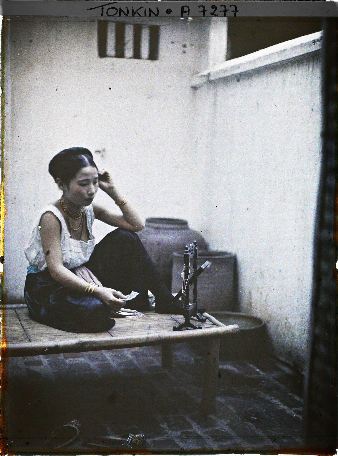 Người đẹp ăn vận hớ hênh, ngồi soi gương trên chõng tre ở sân nhà.