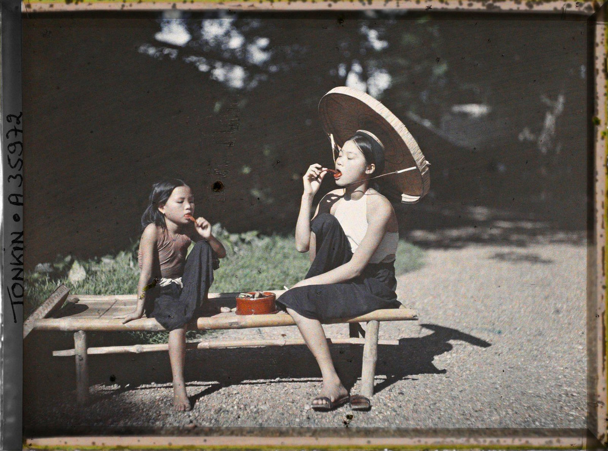 Bé gái và thiếu nữ ngồi trên chõng tre ăn trầu, 1921.