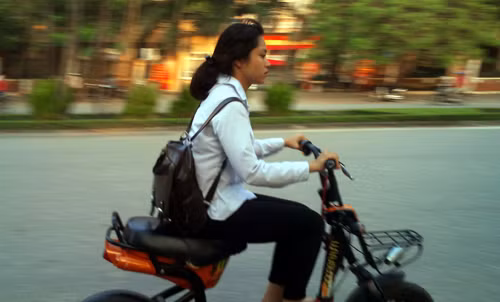 Nữ sinh điều khiển xe đạp điện đầu trần trên phố.