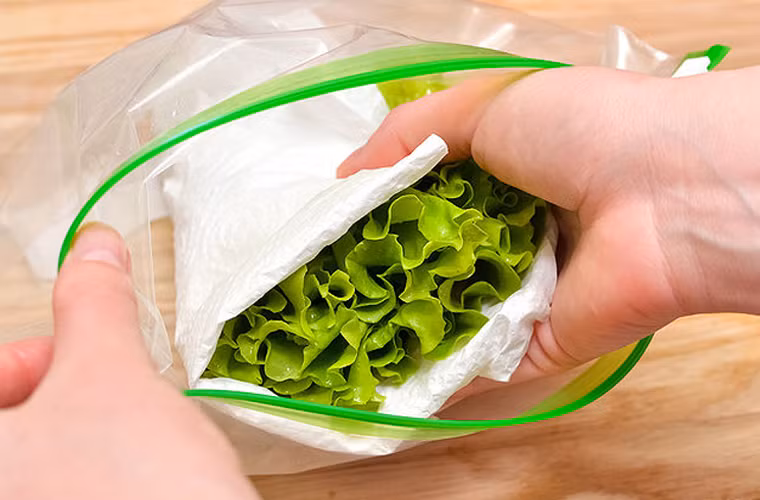 Cho rau đã quấn gọn vào khăn giấy vào túi ni lông nhỏ rồi bọc lại. Nếu túi ni lông không có sẵn khóa kéo, bạn có thể tận dụng băng dính để bịt kín phần miệng túi.