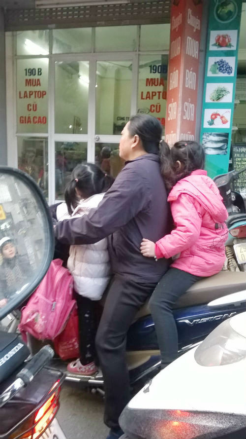 Một người phụ nữ chở hai con nhỏ trên từ trường về, cả ba mẹ con đều không đội MBH. Hình ảnh được ghi tại khu vực gần chợ Bưởi (quận Ba Đình).