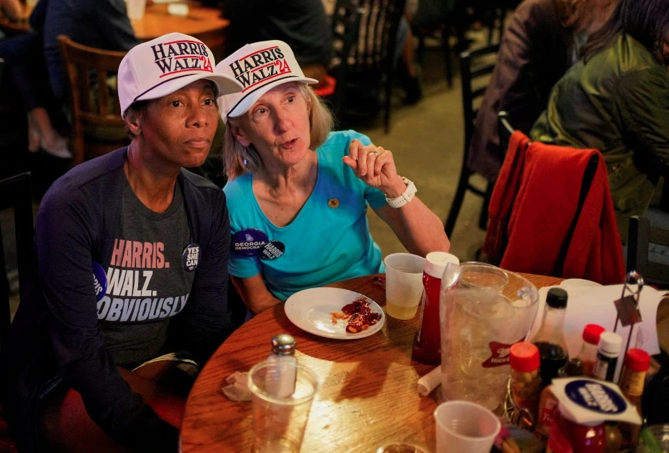 Hai cử tri đội mũ "Harris Walz '24" chăm chú theo dõi kết quả bầu cử sớm tại Manuel's Tavern, ở Atlanta, Georgia.