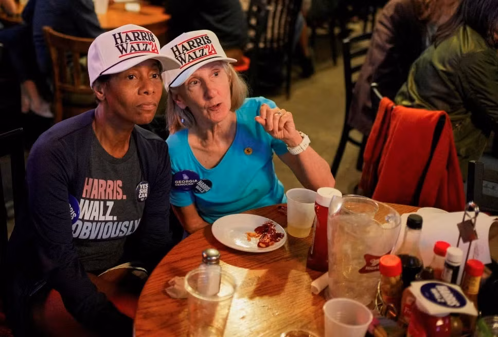 Hai cử tri đội mũ "Harris Walz '24" chăm chú theo dõi kết quả bầu cử sớm tại Manuel's Tavern, ở Atlanta, Georgia.