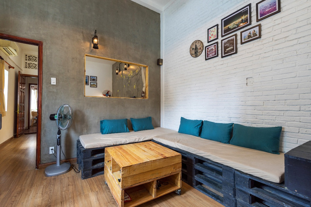 Bức tường trắng được trang trí với các bức tranh kỉ niệm cùng sofa làm từ các tấm pallet khiến phòng khách khá đơn giản nhưng vẫn tạo ấn tượng về sự trẻ trung.