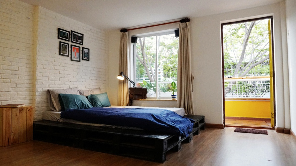 Phòng ngủ nhỏ hơn được bố trí giường ngủ từ gỗ pallet đen nằm sát với ban công nhỏ xinh mang tới sự thông thoáng.