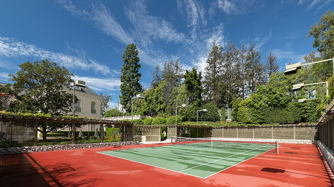 Sân tennis cao cấp, rộng lớn được bao quanh bởi hàng cây cao.