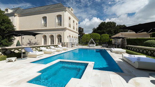 Không gian thư giãn ngoài trời với hồ bơi, bồn tắm nước nóng được bao quanh bởi những chiếc ghế tắm nắng cỡ lớn. Vườn cây xanh mướt được cắt tỉa cẩn thận.