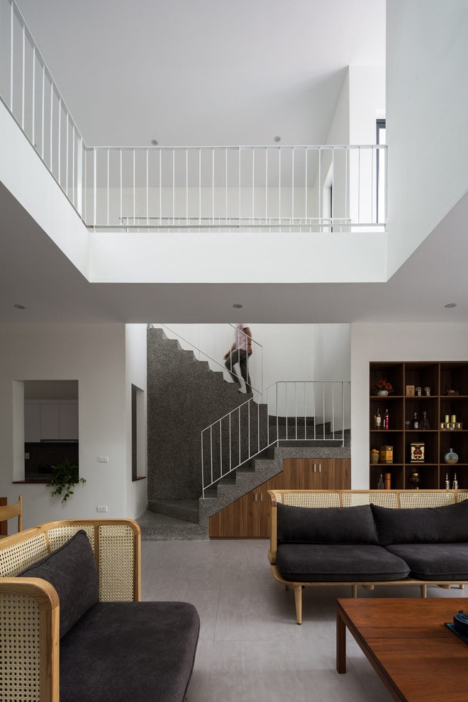 Phòng khách nằm dưới khoảng thông tầng. Các bức tường trắng kết hợp vật liệu bê tông xám của cầu thang tạo nên một tông màu chủ đạo nhã nhặn cho tổng thể nội thất ngôi nhà.