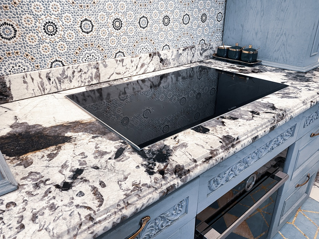 Sắc xanh xám chủ đạo của căn bếp càng được tôn lên với sự kết hợp cùng chất liệu đá Granite vân màu tối nền sáng, ngoài ra còn có gạch ốp trang trí họa tiết làm tăng sự cổ điển. Không chỉ mang tính thẩm mỹ, chất liệu đá Granite cứng, bóng, không bị thấm nước, lau rửa dễ, mặc dù giá thành cao nhưng bền.