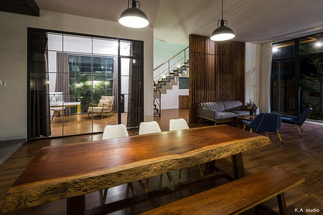 Chiếc bàn ăn làm từ gỗ nguyên tấm khổ lớn là sự đối lập với phòng khách gọn gàng. Phòng làm việc của chủ nhà được ngăn bằng vách kính và có rèm kéo đảo bảo riêng tư.