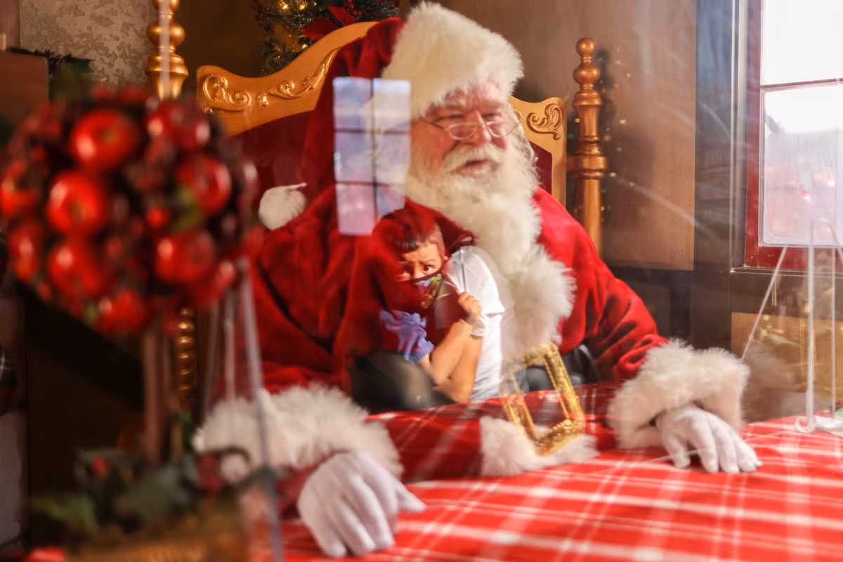 Đằng sau lớp khẩu trang, kính chống giọt bắn và vách ngăn nhựa, các ông già Noel vẫn đang tiếp tục gặp mặt các em nhỏ. Mọi năm, lũ trẻ sẽ ngồi lên lòng, nói chuyện với ông hoặc đứng sát gần. Năm nay, điều này là không thể vì cần giữ khoảng cách tối thiểu. Trong ảnh, ông Panchito Vicente (74 tuổi) đang ngồi sau tấm ngăn nhựa tại trung tâm thương mại Citadel Outlet ở California (Mỹ).
