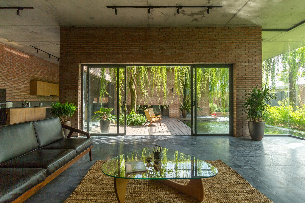 Tầng trệt là khu vực sinh hoạt chính của gia đình. Từ ngoài vào trong, xuyên qua bức tường gạch đỏ là một lớp rèm được làm từ cây xanh bao phủ khắp ngôi nhà.