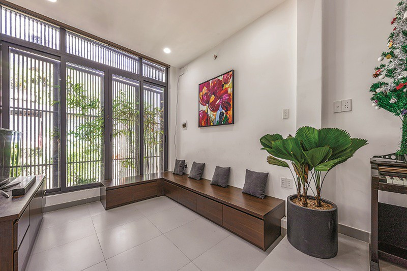 Ở tầng 1, là một không gian liên thông giữa phòng khách và bếp. Lối vào và để xe được tách riêng một bên so với phòng khách vì mặt tiền rộng. Phòng khách mở cửa ra khoảng sân phía trước. Để khắc phục nhược điểm hạn chế về diện tích, chủ nhà không sử dụng bộ sofa hay salon bề thế mà chỉ dùng một hệ thống ghế ngồi bằng kệ gỗ để tiếp khách.