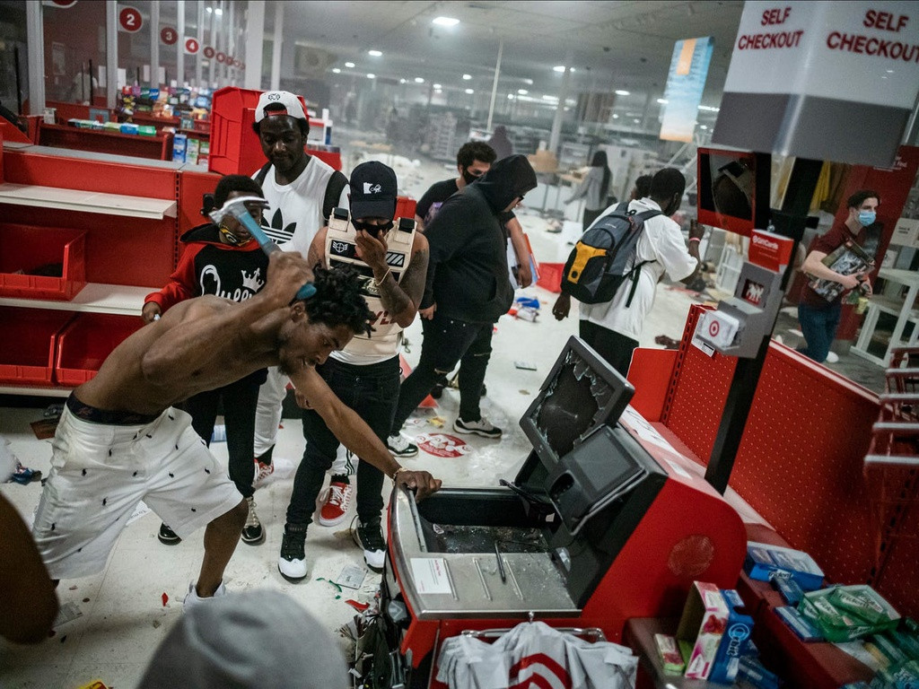 Không chỉ vét sạch hàng hoá, một bộ phận người biểu tình có hành vi đập phá trang thiết bị khác của các cửa hàng. Trong ảnh là một người đàn ông đang dùng búa phá huỷ máy đếm tiền trong một cửa hàng The Target. Ảnh: Getty Images.