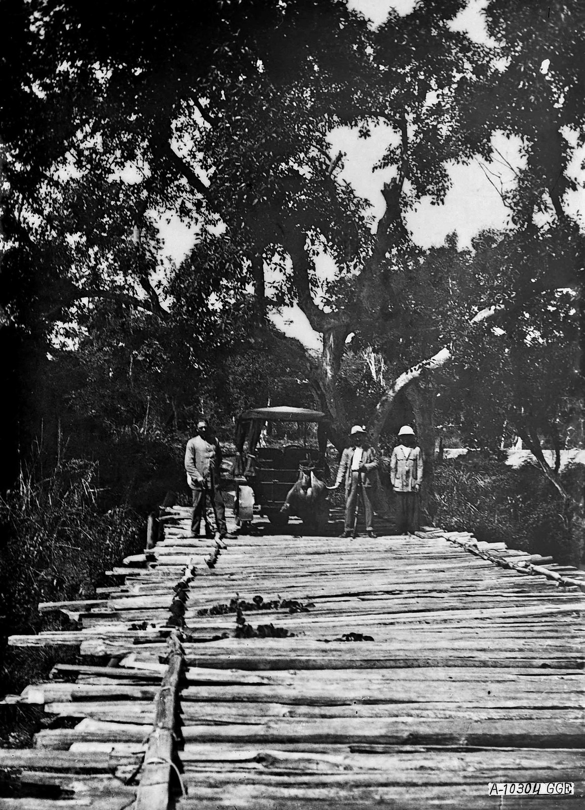 Nhóm đi săn đứng trước chiếc ô tô dừng trên cây cầu gỗ. Trên xe treo con vật săn được.