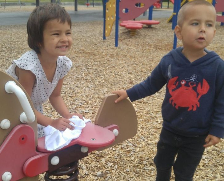 Bé gái lấy khăn lau chiếc ghế bập bênh bị ướt, trước khi em trai ngồi lên.