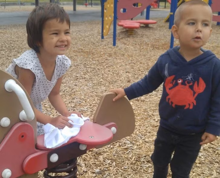 Bé gái lấy khăn lau chiếc ghế bập bênh bị ướt, trước khi em trai ngồi lên.