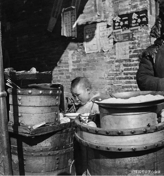 Trong ảnh, một người bán hàng rong đang bận rộn chuẩn bị đồ ăn cho khách, trong khi đứa con của anh ngồi bên cạnh ăn sáng một cách ngon lành.