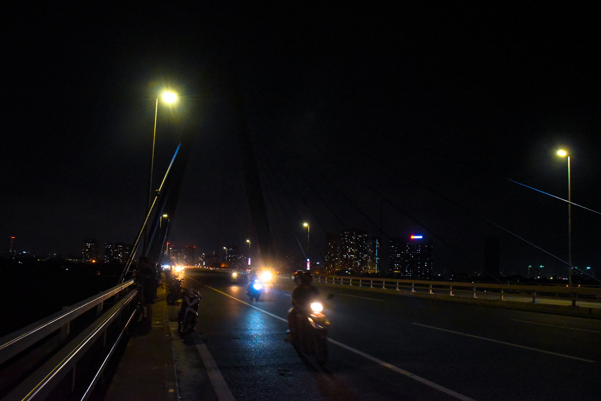 Ở phía Bắc Hà Nội, cầu Nhật Tân vào những ngày cắt giảm điện không còn lung linh với hệ thống đèn đầy màu sắc như trước. Người dân đi qua cầu chủ yếu phụ thuộc vào ánh sáng từ dòng xe cộ và 50% đèn đường còn vận hành.