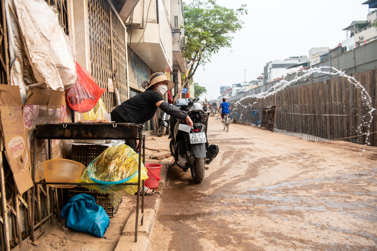 Sạp hàng của bà Loan từ ngày có dự án cũng vơi khách dần. Người phụ nữ phải liên tục hất nước cho lớp bụi không bị những phương tiện đi qua cuốn bay lên.