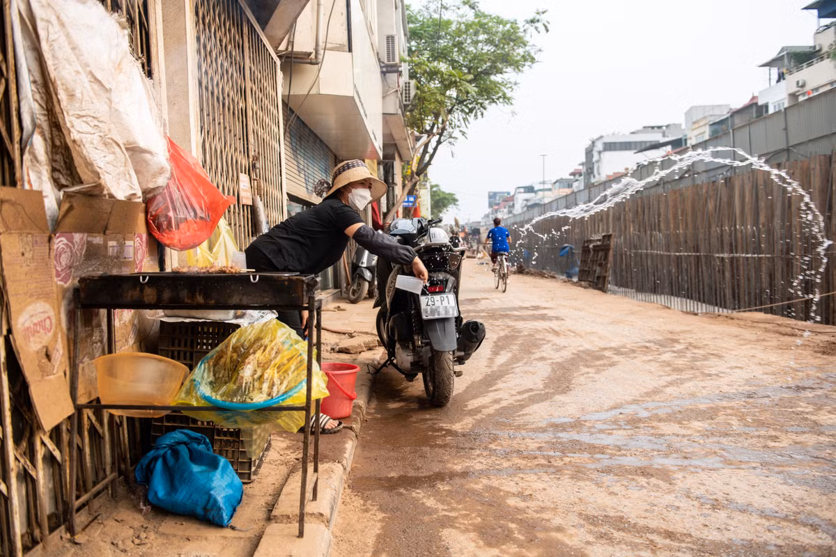 Sạp hàng của bà Loan từ ngày có dự án cũng vơi khách dần. Người phụ nữ phải liên tục hất nước cho lớp bụi không bị những phương tiện đi qua cuốn bay lên.