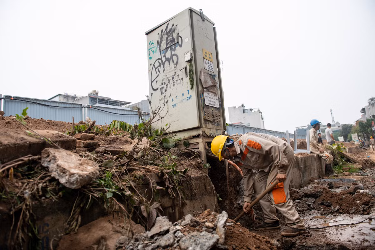 Công nhân di dời hệ thống hạ tầng kỹ thuật để đoạn đê cũ bằng đất nhanh chóng được phá bỏ trước thời hạn mùa lũ phải dừng thi công.