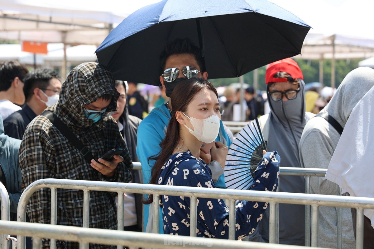 Nhiều người mang ô, mặc kín mít, đeo kính râm đứng xếp hàng dưới cái nắng gay gắt. Ảnh: Như Ý.