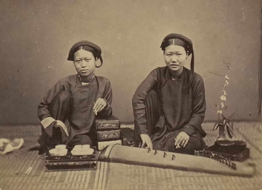 Ảnh chân dung hai thiếu nữ trong trang phục áo dài khăn đóng truyền thống. Đặt trước mặt người phụ nữ trẻ ở bên phải, chúng ta có thể thấy một cây đàn tranh, một nhạc cụ truyền thống của Việt Nam.