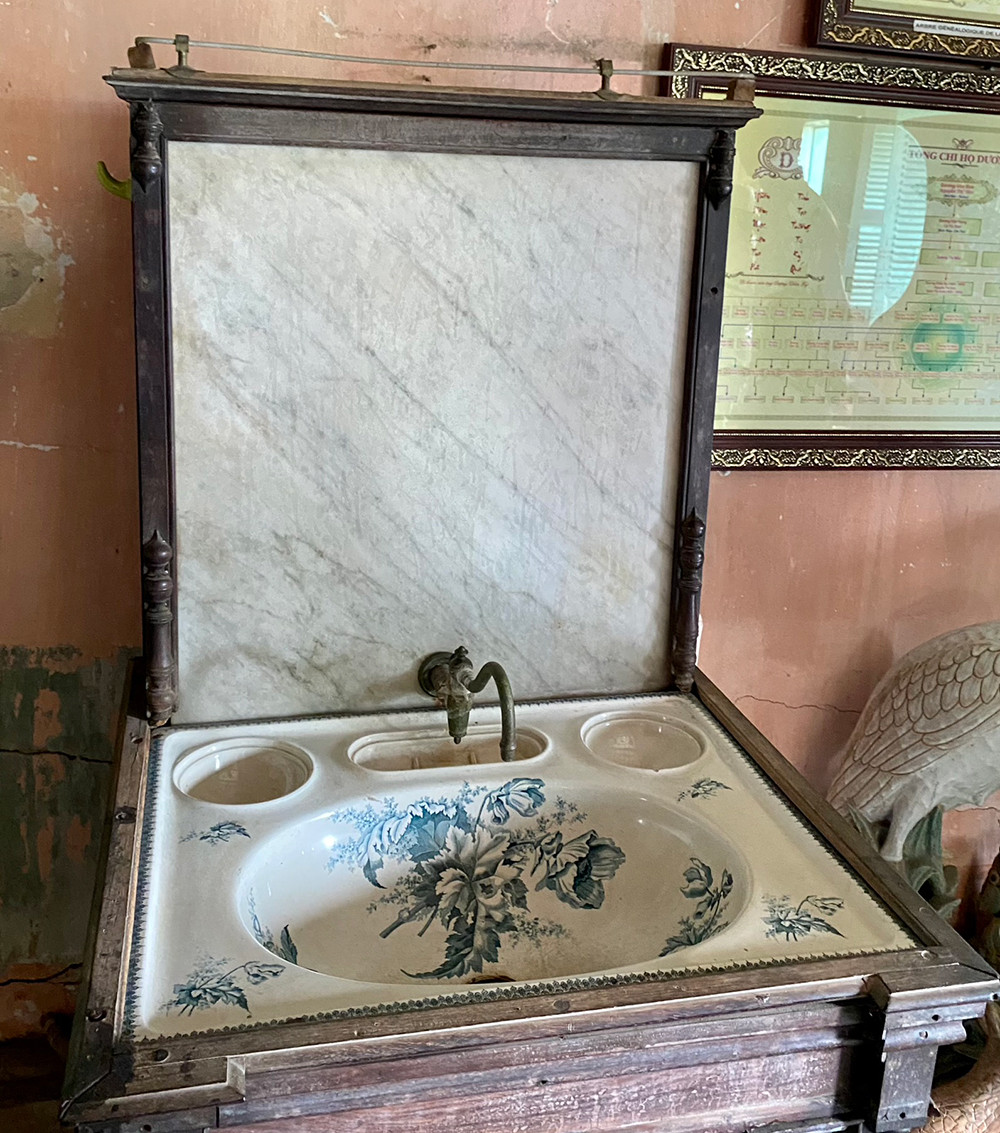 Chiếc bồn rửa tay bằng men sứ trắng, hoa xanh đặt trên bục gỗ độc đáo được mua về từ Pháp