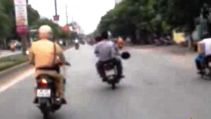 CSGT mặc sắc phục đang đuổi theo hai đối tượng không đội mũ bảo hiểm lạng lách trước mặt.