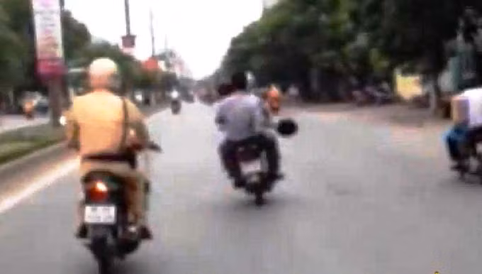CSGT mặc sắc phục đang đuổi theo hai đối tượng không đội mũ bảo hiểm lạng lách trước mặt.