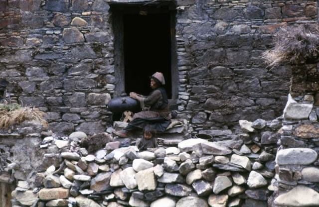 Người phụ nữ Tây Tạng khuấy sữa bò yak để làm bơ bên cửa nhà.