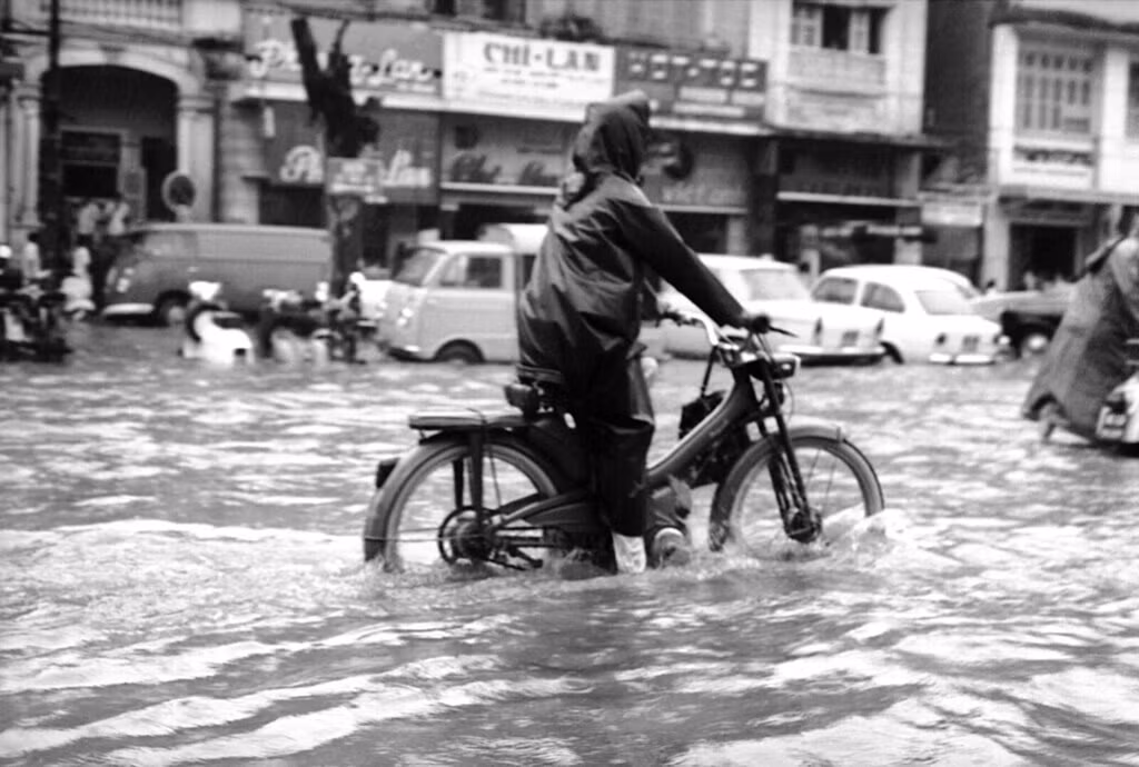 Người phụ nữ ngồi xe moped "lặn lội" giữa dòng nước. Ảnh: Eddie Adams.