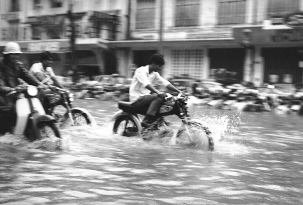 Các thanh niên cưỡi xe gắn máy lướt đi trên sóng nước Sài thành. Ảnh: Eddie Adams.