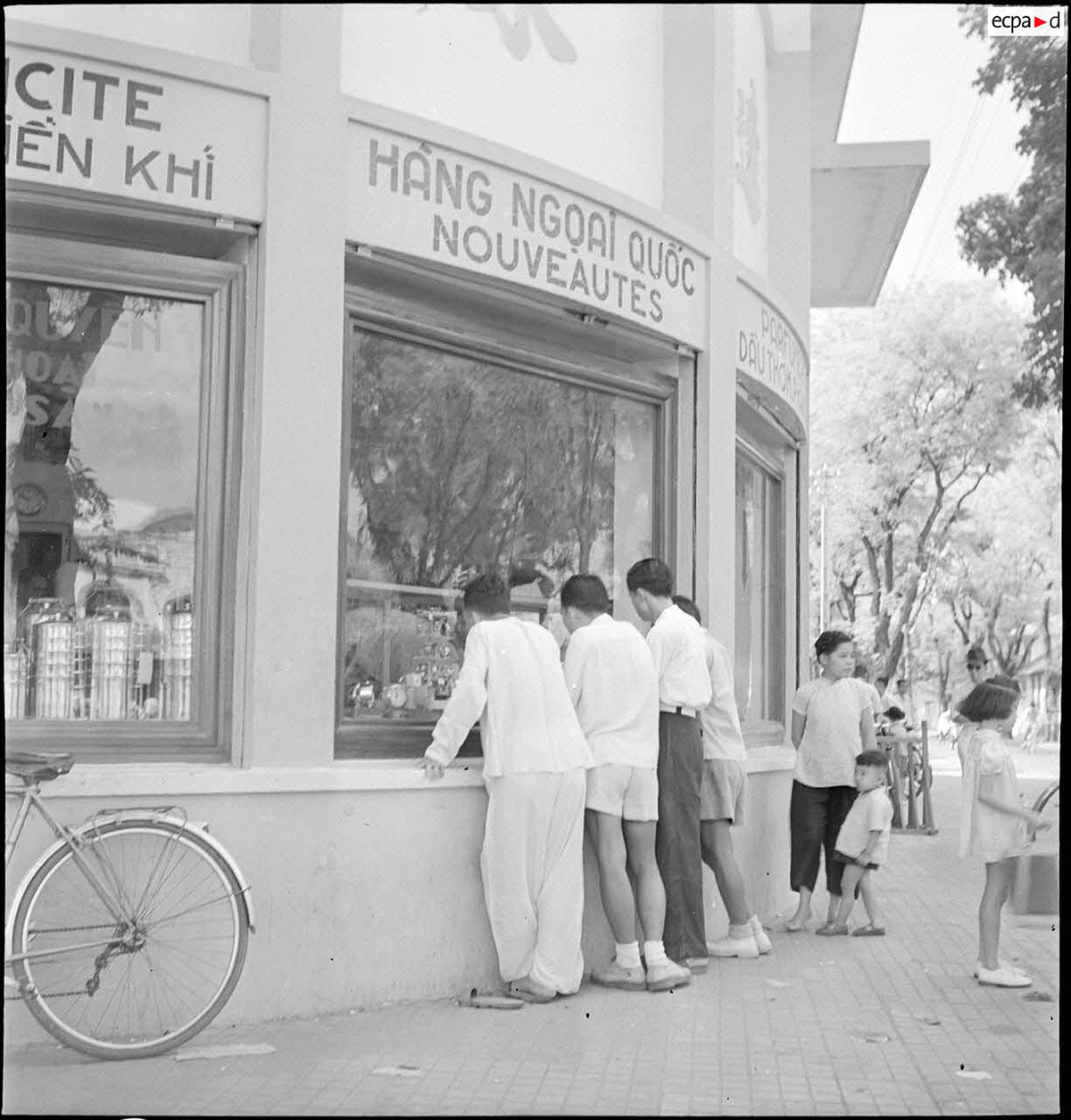 Khách qua đường dừng lại ngắm các mặt hàng ngoại quốc được trưng bày phía sau ô cửa kính của cửa hàng bách hóa Viễn Đông. Ảnh: Auteur inconnu/ECPAD/Défense.