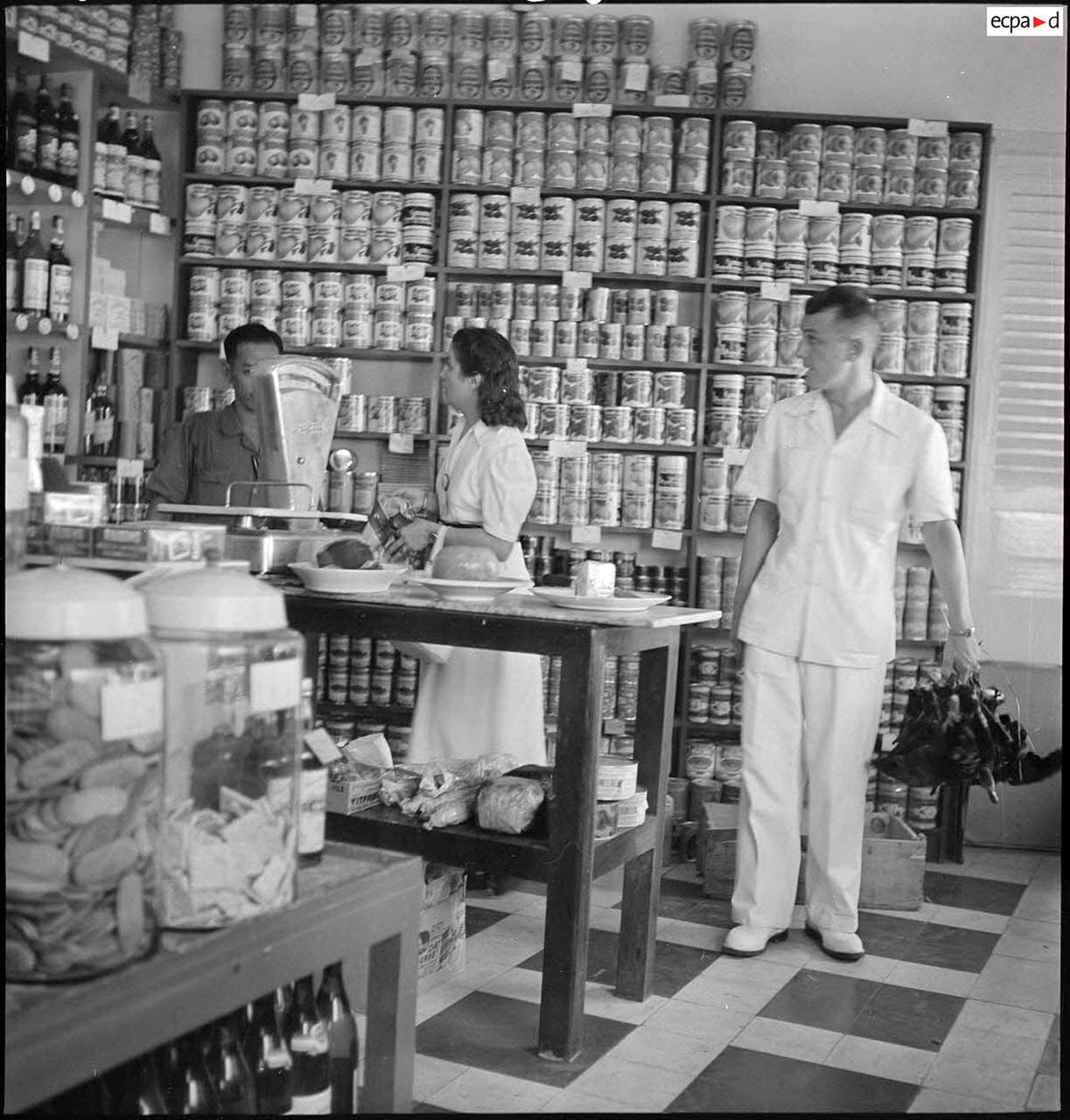 Cặp đôi người nước ngoài ở quầy bán sản phẩm đóng hộp. Ảnh: Auteur inconnu/ECPAD/Défense.