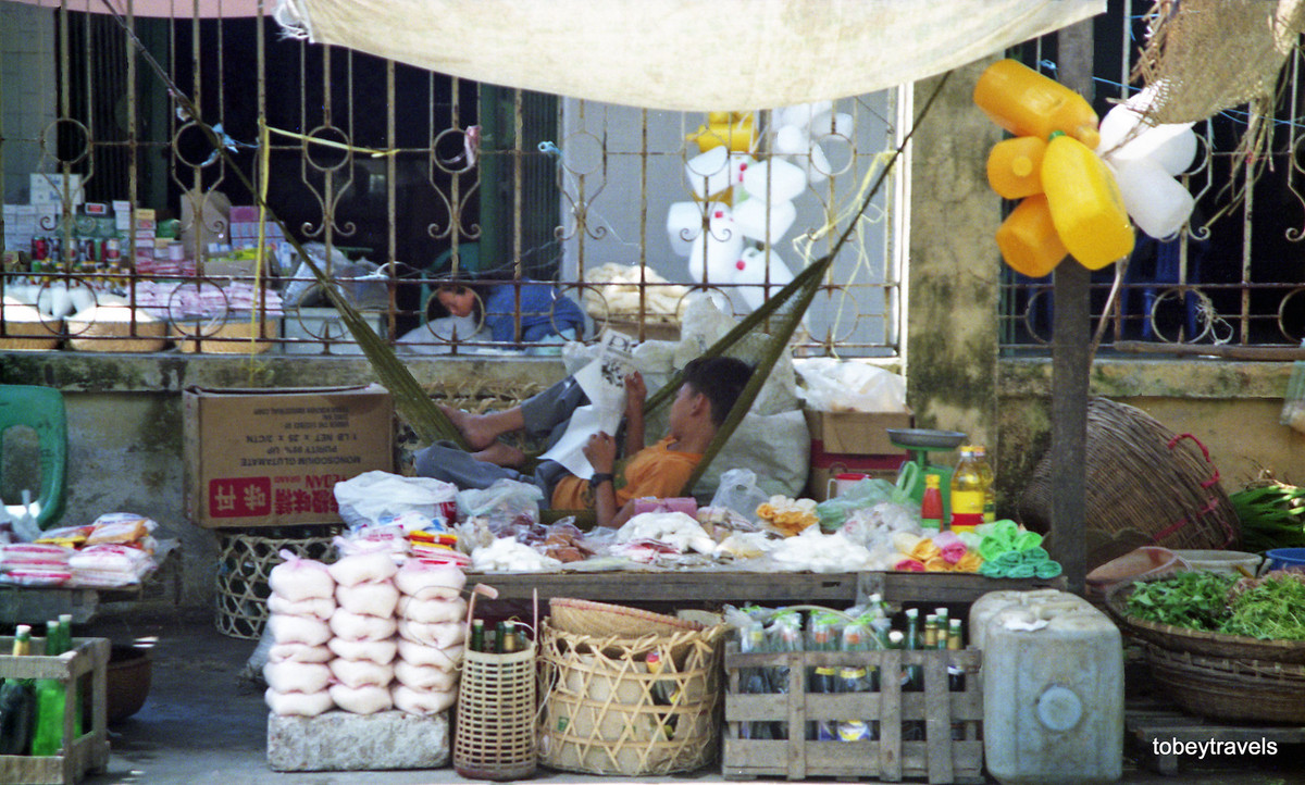 Một cậu bé nằm võng khi trông cửa hàng.