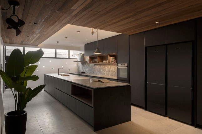 Trong khi trần nhà cao và tông màu trắng được thiết kế bao phủ hầu hết các khu vực khác của căn nhà, thì trần gỗ hạ thấp và tông màu tối lại được lựa chọn cho nhà bếp. Điều này đem đến sự tương phản thú vị và góp phần mang lại bầu không khí ấm cúng hơn cho không gian sum vầy của gia chủ.