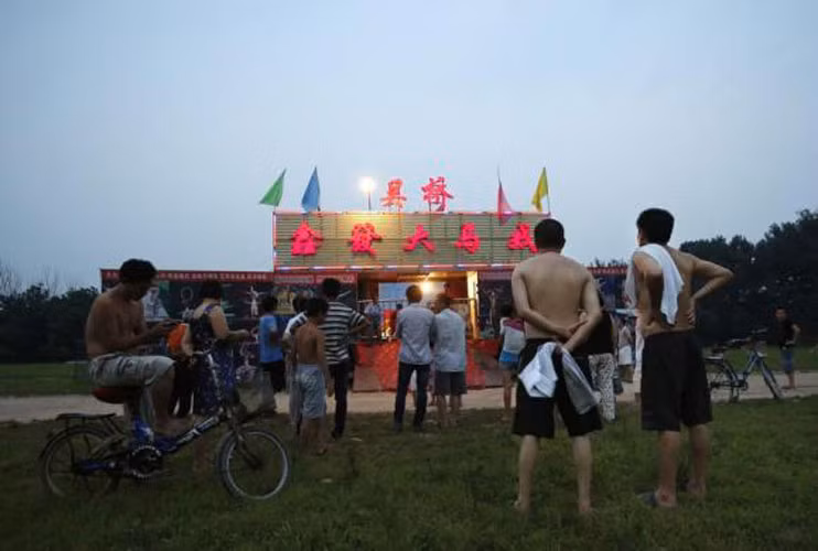 Những người dân lao động nghèo sống trong khu dành cho lao động nhập cư xem gánh xiếc rong biểu diễn ở Bắc Kinh ngày 17/7.