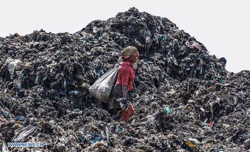 Một phụ nữ đeo chiếc bị to đựng rác sau lưng giữa núi rác khổng lồ, cao ngất ở bãi rác Dandora, thủ đô Nairobi.
